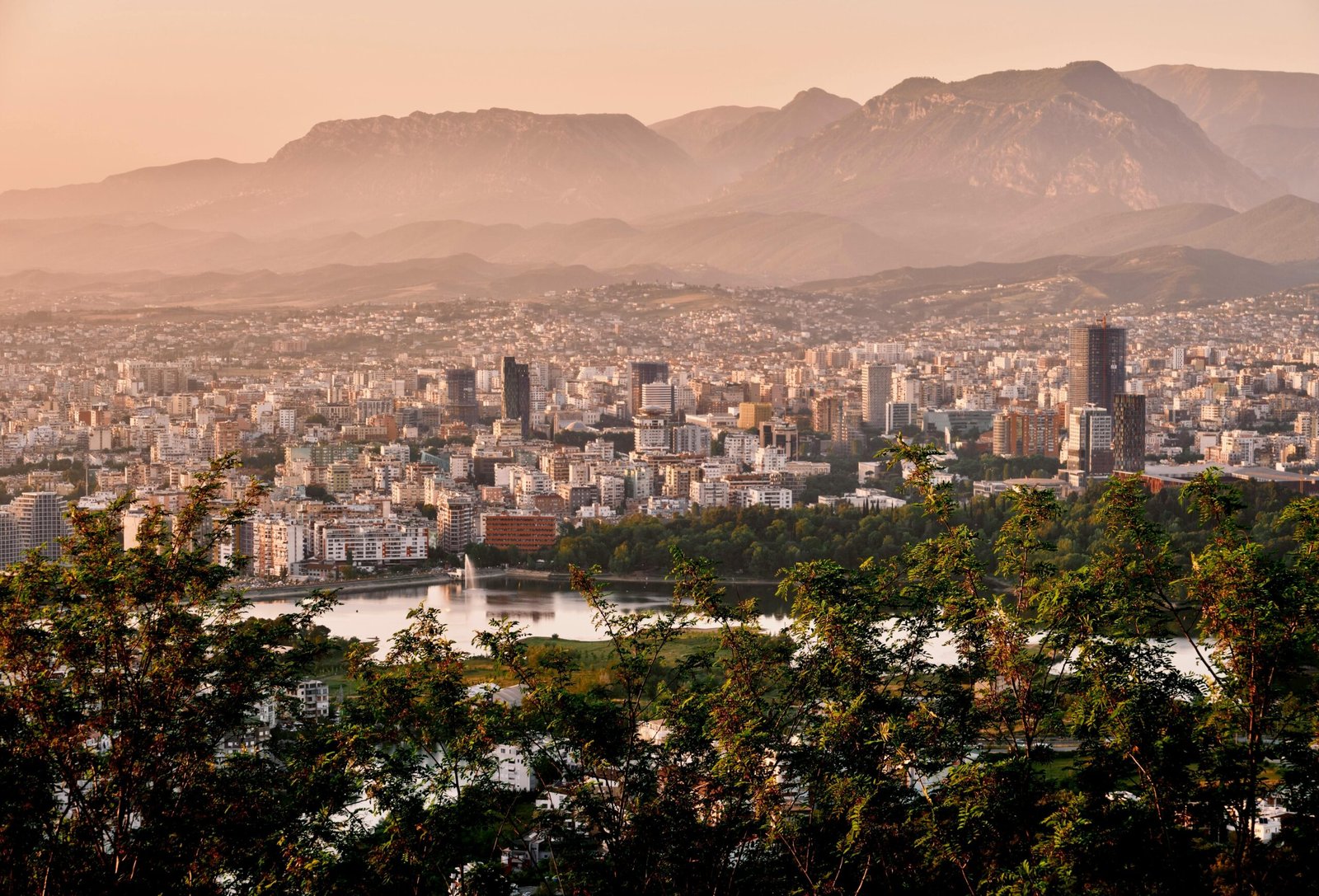 A stunning aerial view of Tirana's skyline framed by mountains and lush greenery during sunset.